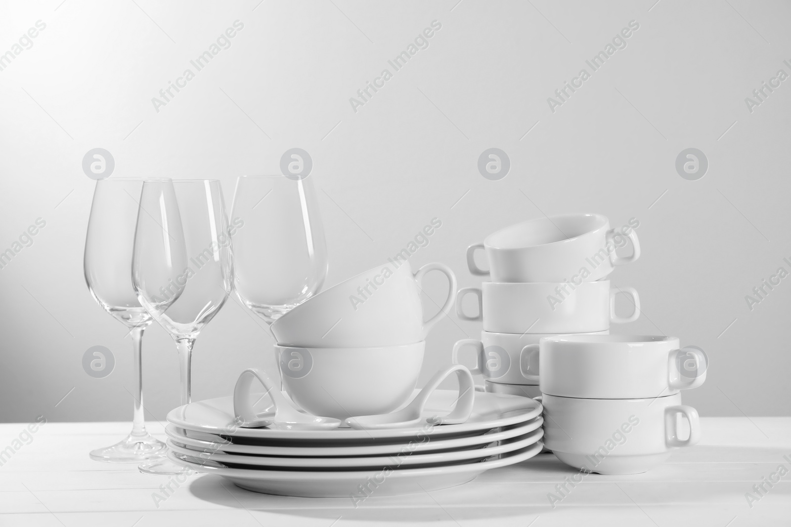 Photo of Set of clean dishware and glasses on white wooden table against light background