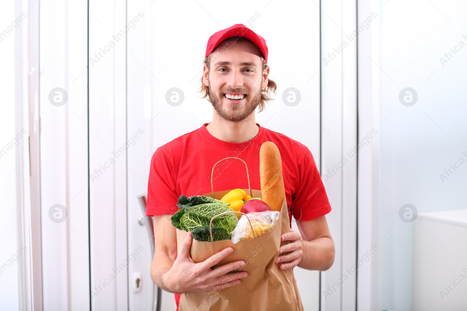 Photo of Delivery man holding paper bag with food products indoors