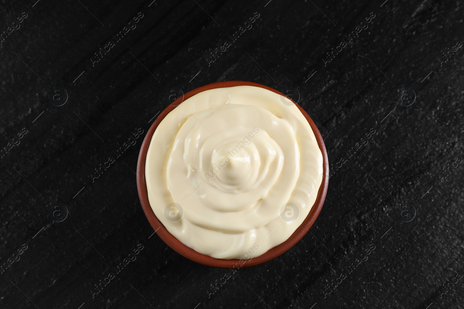 Photo of Fresh mayonnaise sauce in bowl on black table, top view