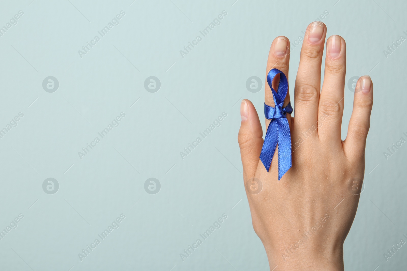 Photo of Woman with blue ribbon on finger against light background, closeup. Symbol of social and medical issues