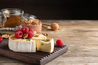 Photo of Brie cheese served with raspberries, walnuts and honey on wooden table. Space for text