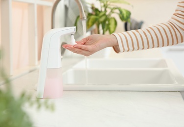 Woman using automatic soap dispenser in kitchen, closeup