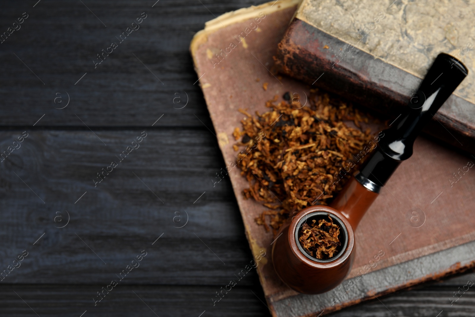 Photo of Smoking pipe, dry tobacco and old books on wooden table, top view. Space for text