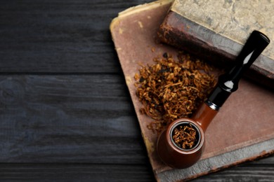 Photo of Smoking pipe, dry tobacco and old books on wooden table, top view. Space for text