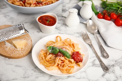Tasty pasta with cheese, tomato sauce and basil on white marble table
