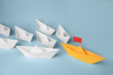 Photo of Group of paper boats following yellow one on light blue background. Leadership concept