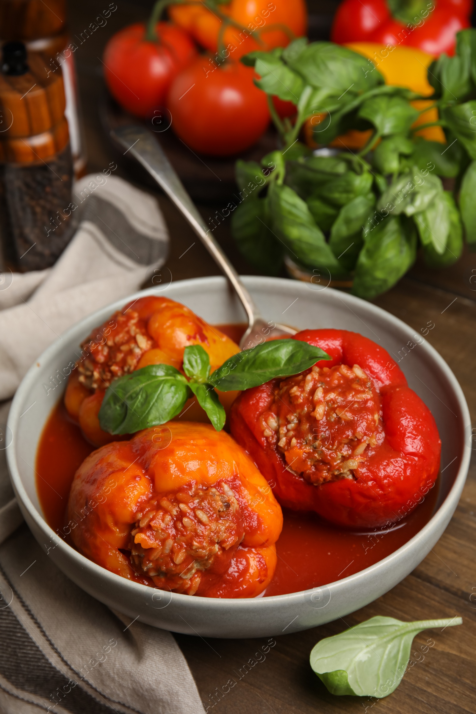 Photo of Delicious stuffed peppers with basil in bowl on wooden table