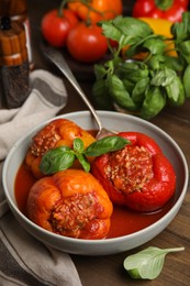 Photo of Delicious stuffed peppers with basil in bowl on wooden table