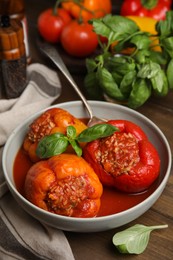 Delicious stuffed peppers with basil in bowl on wooden table