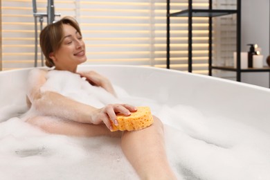 Happy woman taking bath with foam in tub indoors, selective focus