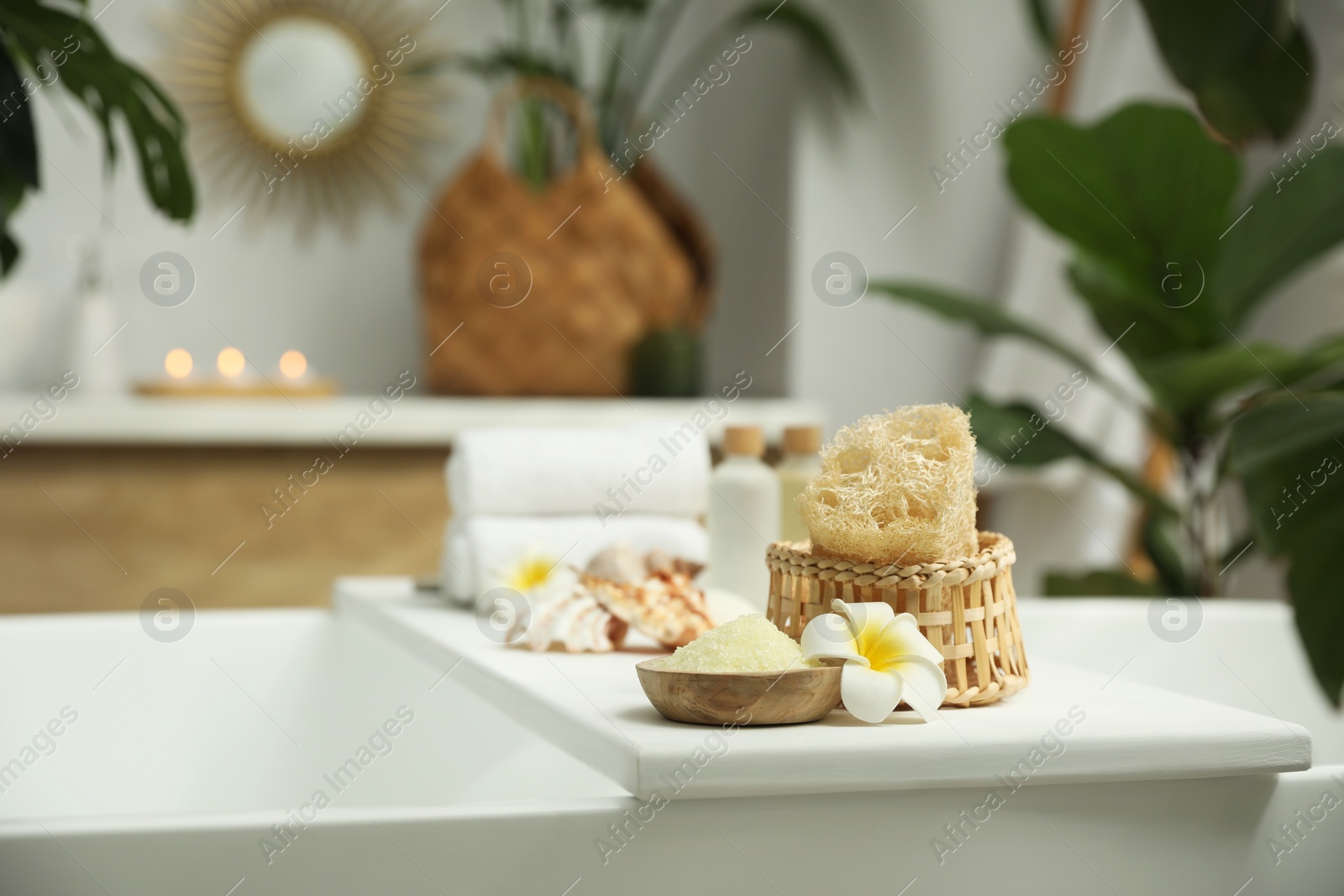 Photo of Bath tray with spa products and plumeria flower on tub in bathroom, space for text