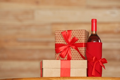 Bottle of wine and gift boxes on table against blurred background. Space for text