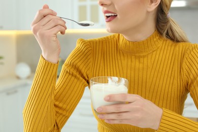 Happy woman eating tasty yogurt in kitchen, closeup