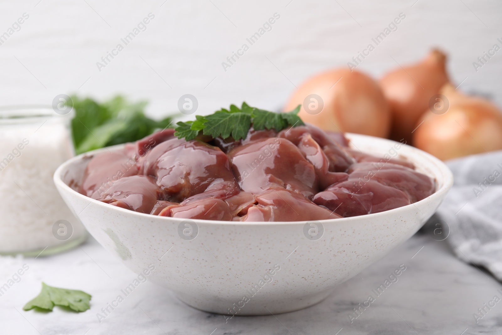 Photo of Bowl of raw chicken liver with parsley on white table, closeup