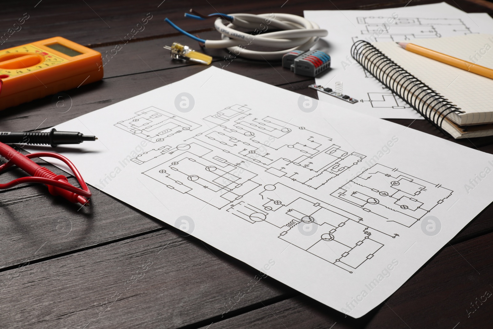 Photo of Wiring diagrams, office stationery, wires and digital multimeter on wooden table