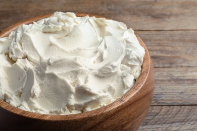 Photo of Bowl of tasty cream cheese on wooden table, closeup