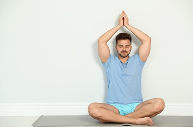 Photo of Young man practicing zen yoga near wall indoors