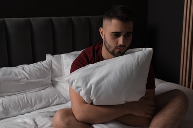 Sad man hugging pillow on bed at home. Space for text