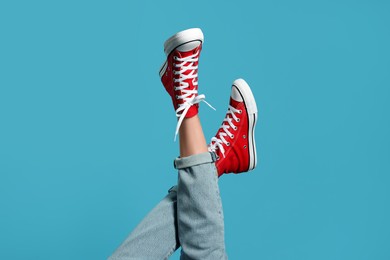 Photo of Woman in stylish gumshoes on light blue background, closeup