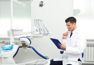 Portrait of professional male dentist with clipboard in clinic. Space for text