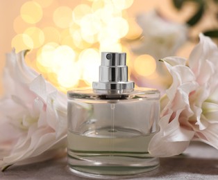 Photo of Bottle of perfume and beautiful lily flowers on table against beige background with blurred lights, closeup