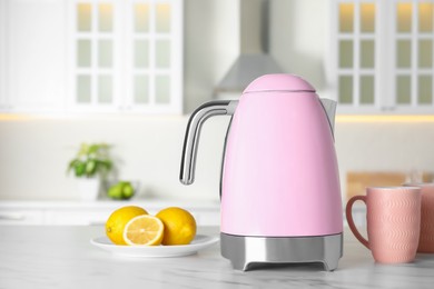 Photo of Modern electric kettle, cups and lemons on table in kitchen