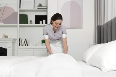 Photo of Young chambermaid making bed in hotel room