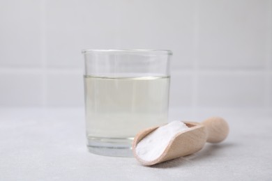 Photo of Vinegar in glass, baking soda and wooden scoop on light table