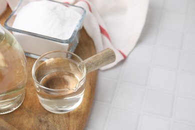 Photo of Vinegar in glass saucepan and baking soda on white tiled table, space for text