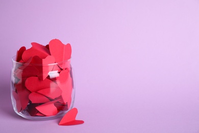 Photo of Red paper hearts in jar on violet background. Space for text
