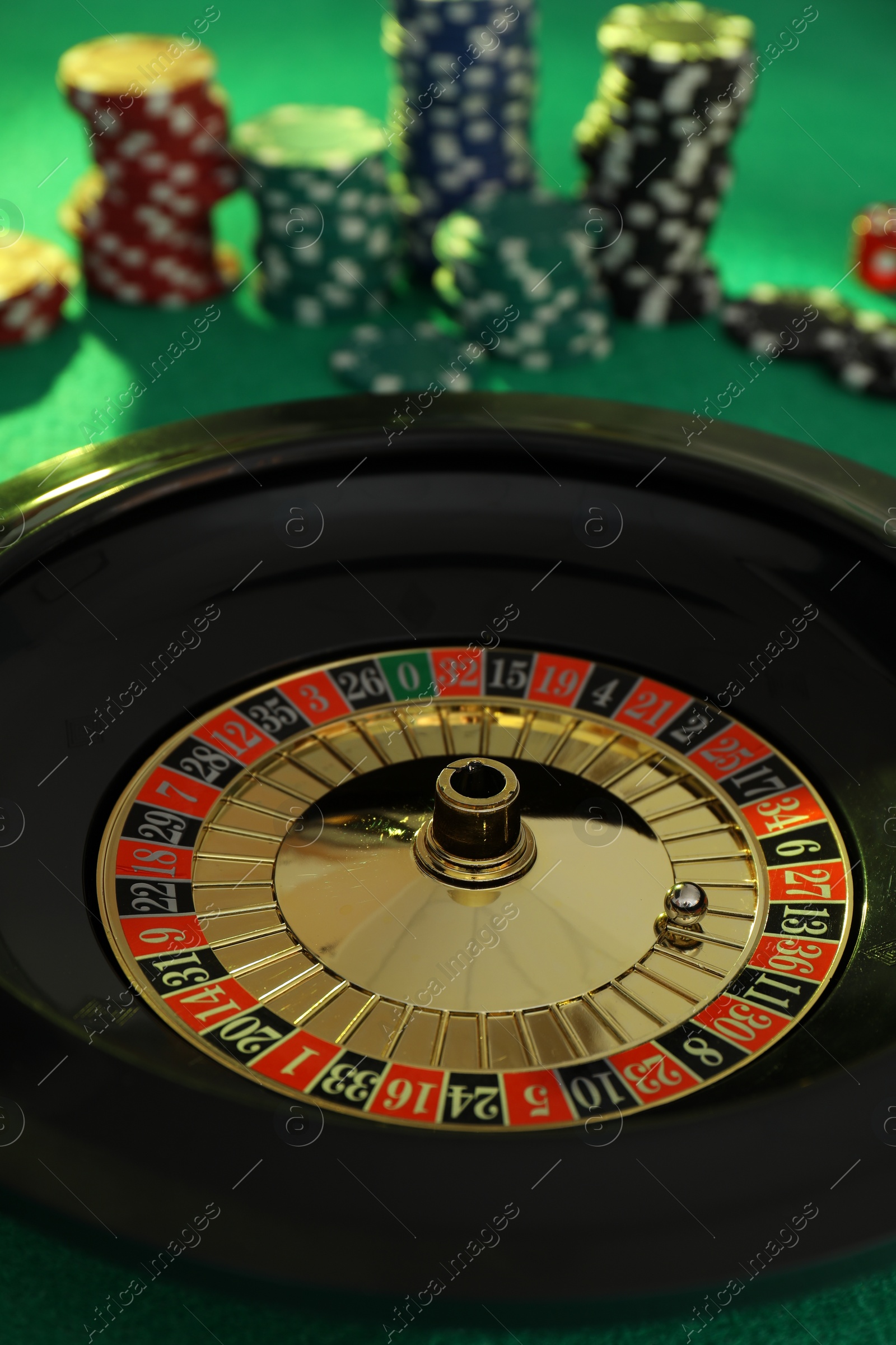 Photo of Roulette wheel with ball and chips on green table, closeup. Casino game