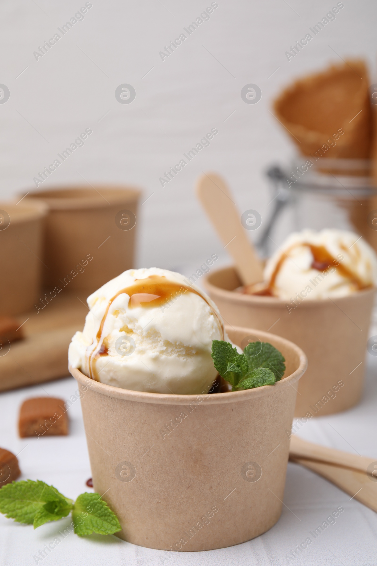 Photo of Scoops of ice cream with caramel sauce, mint leaves and candies on white tiled table, closeup