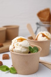 Photo of Scoopsice cream with caramel sauce, mint leaves and candies on white tiled table, closeup