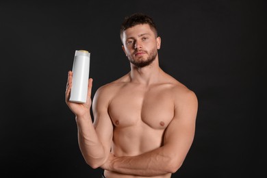 Photo of Shirtless young man holding bottle of shampoo on black background