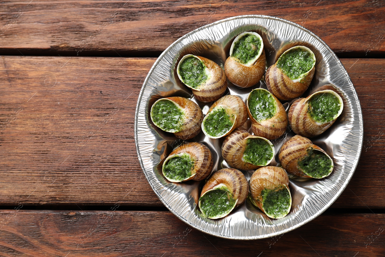 Photo of Delicious cooked snails on wooden table, top view. Space for text