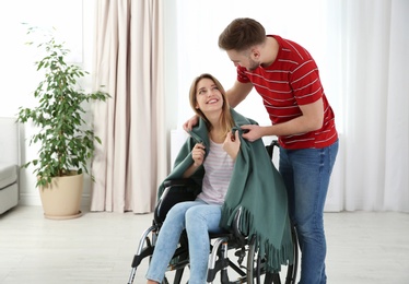 Man covering woman in wheelchair with plaid at home. Helping disabled