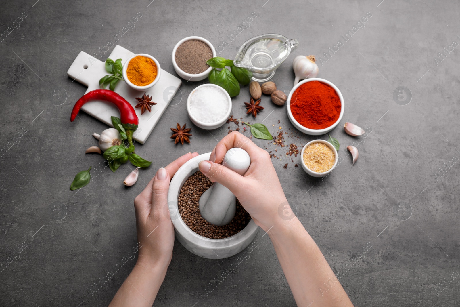 Photo of Woman grinding coriander at grey table, top view