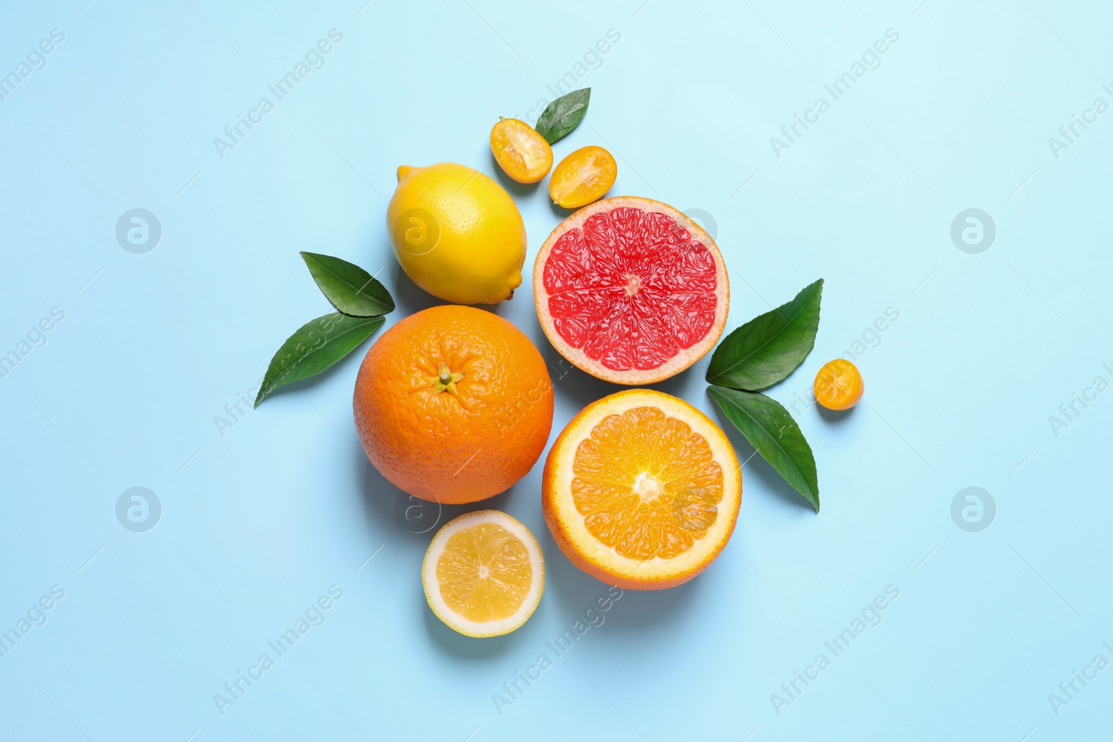 Photo of Fresh juicy citrus fruits with green leaves on light blue background, flat lay