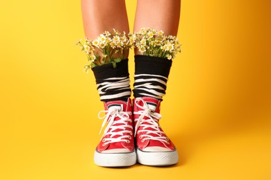 Photo of Woman with beautiful tender chamomile flowers in socks on yellow background, closeup
