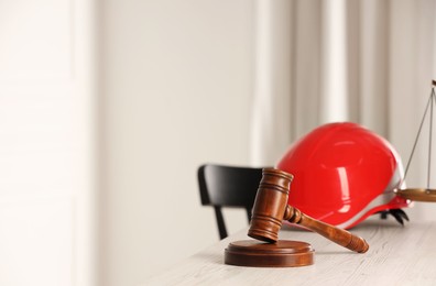 Law concept. Gavel and red hard hat on white wooden table, space for text