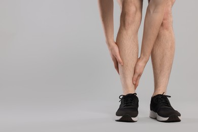 Photo of Man suffering from leg pain on grey background, closeup. Space for text