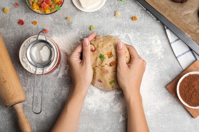 Photo of Woman holding unbaked cookie with candied fruits at grey table, top view