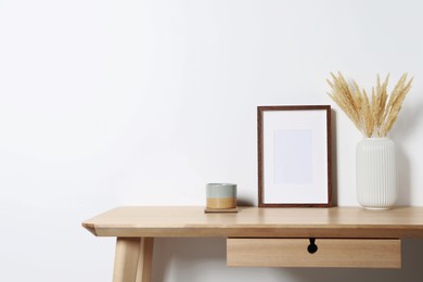 Empty photo frame, cup and vase with dry decorative spikes on wooden table. Mockup for design