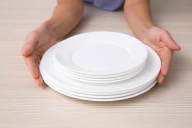 Photo of Woman with stack of clean dishes at table, closeup