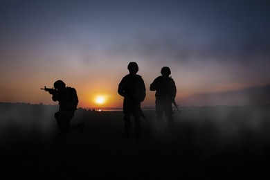 Image of Silhouettes of soldiers with machine guns on battlefield at sunset