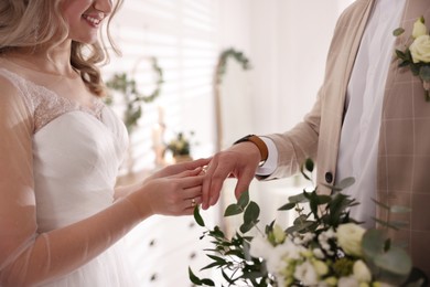 Photo of Groom and bride exchanging wedding rings indoors, closeup view