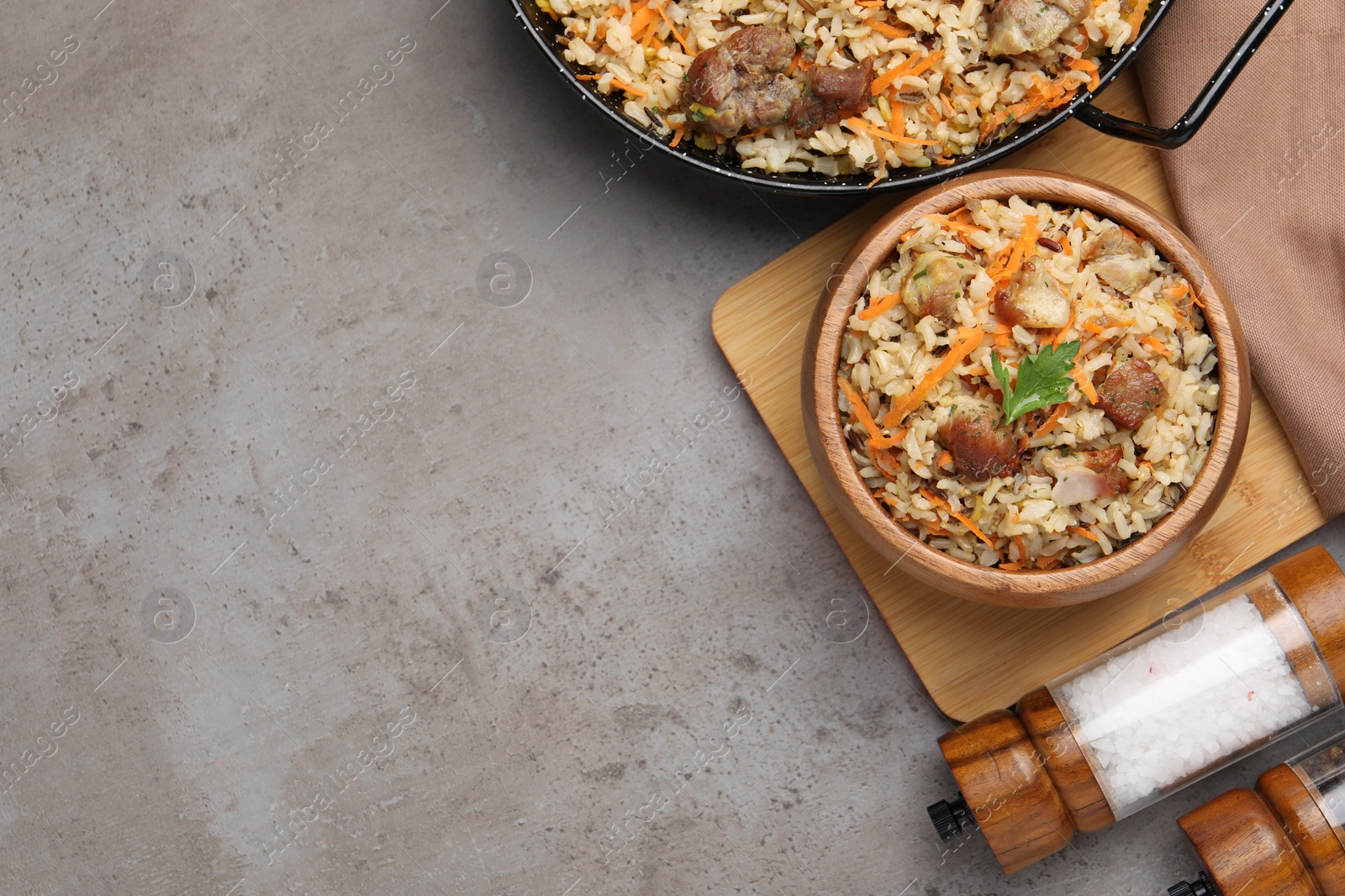Photo of Delicious pilaf with meat and carrot on grey textured table, flat lay. Space for text