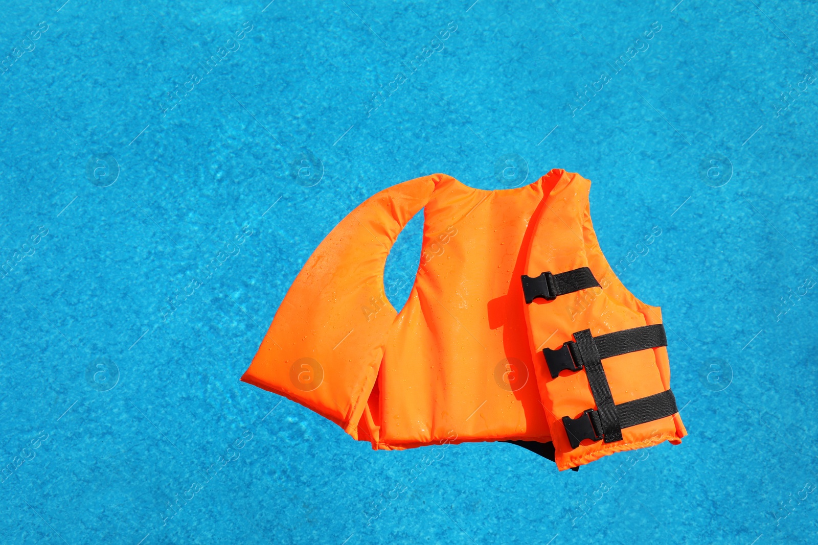 Photo of Bright orange life jacket floating in swimming pool, top view