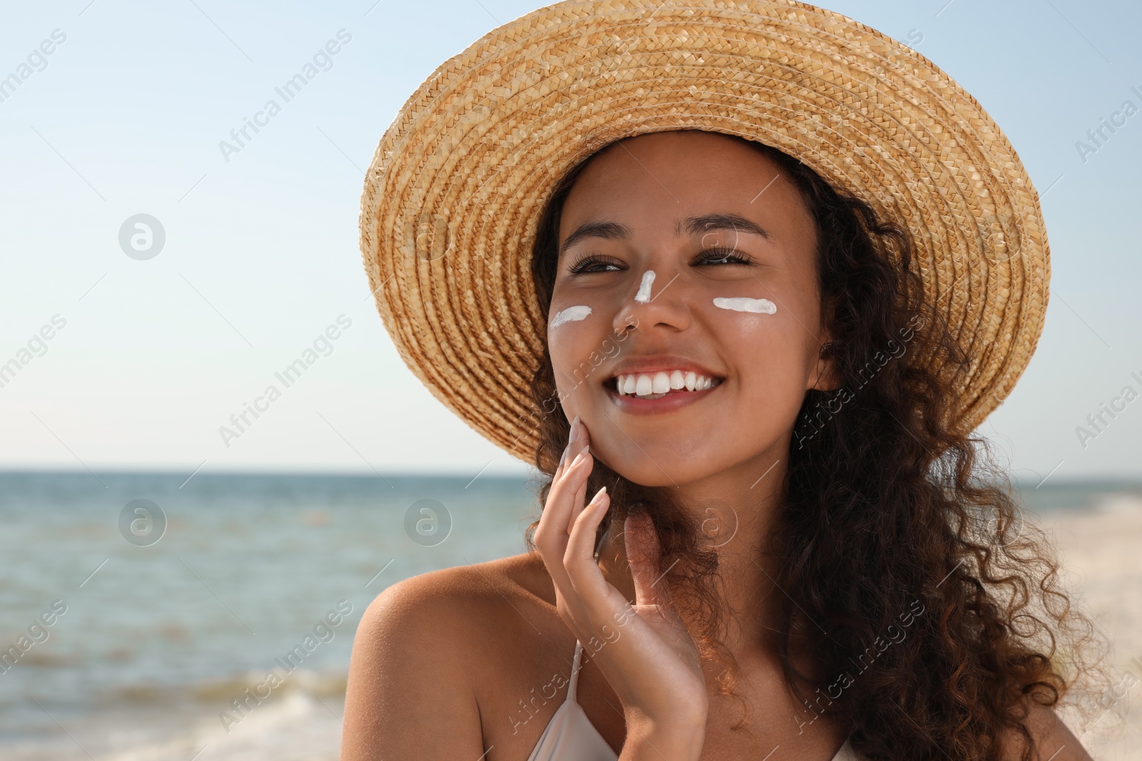 Photo of Beautiful African American woman with sun protection cream on face at beach