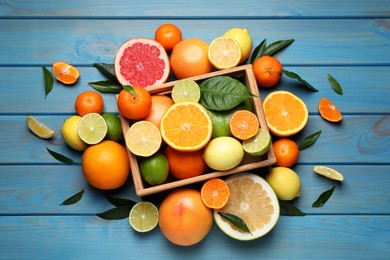 Photo of Different ripe citrus fruits with green leaves on light blue wooden table, flat lay